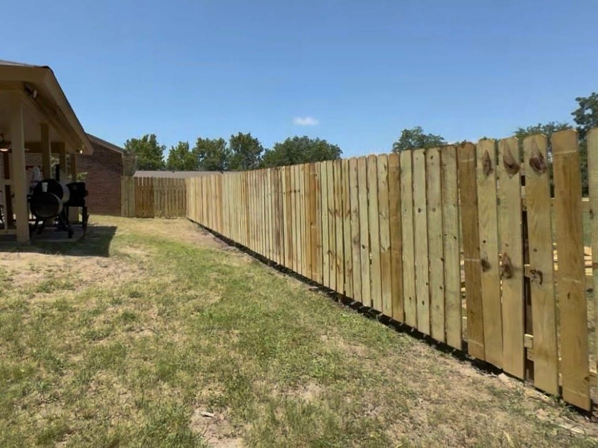 A newly built wooden dog-ear privacy fence running along the back of a Delta property, with a gate